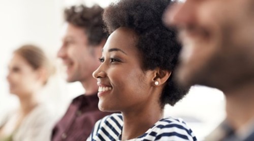 Four people sitting in a row with focus on the individual in the middle wearing striped shirt