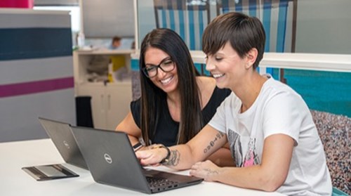 Two employees sitting in front of laptops pointing at the screen