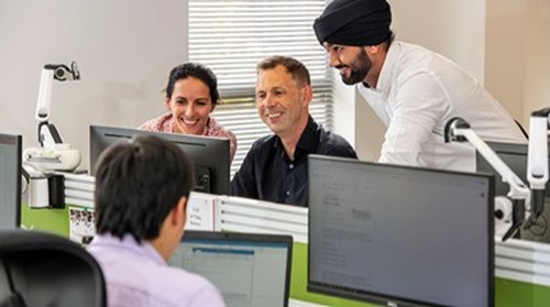 Man with black turban stands next to two colleagues looking at computer screen