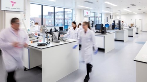 Scientists wearing white lab-coats walk around an RB laboratory