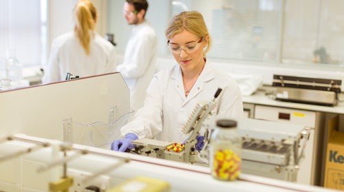 Blonde scientist in lab looks down intently at microscope