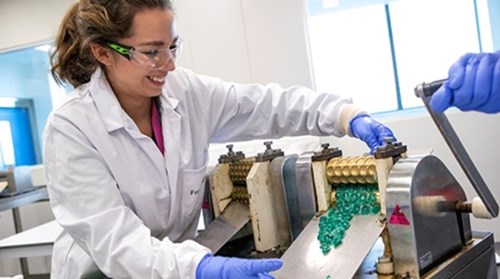 Smiling lab technician working in a lab operating a Strepsil pressing machine