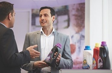 Man in grey suit showing bottle of Woolite to another man in suit