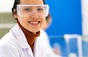 Scientist in a lab wearing protective goggles and white lab-coat