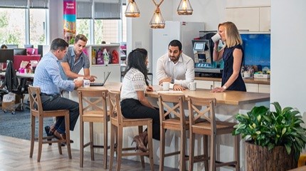 Colleagues sitting and standing around a table in an office kitchen