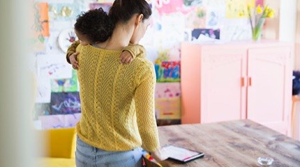 Parent standing up holding a baby looking at an iPad in a nursery