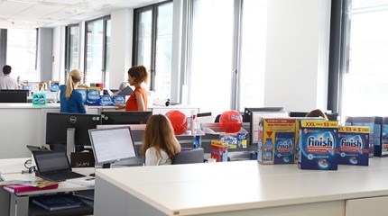 Person sitting in an office facing a computer with three different boxes of Finish on the cupboard behind her