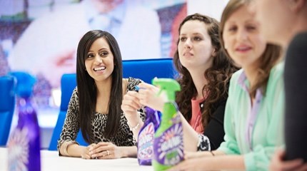 Cillit Bang employees sit around a table with purple and green bottles of Cillit Bang on it