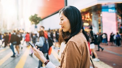 Busy street crossing person with beige jacket looks at their phone 