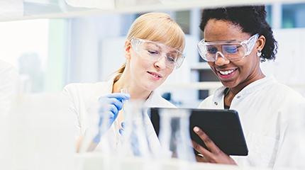 Two RB scientists wearing white lab coats look at a tablet while working in a laboratory