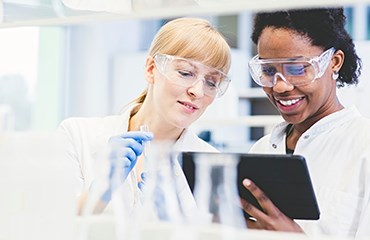 Two RB scientists wearing white lab coats look at a tablet while working in a laboratory