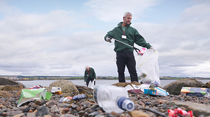 Two volunteers picking up plastic waste on a beach 