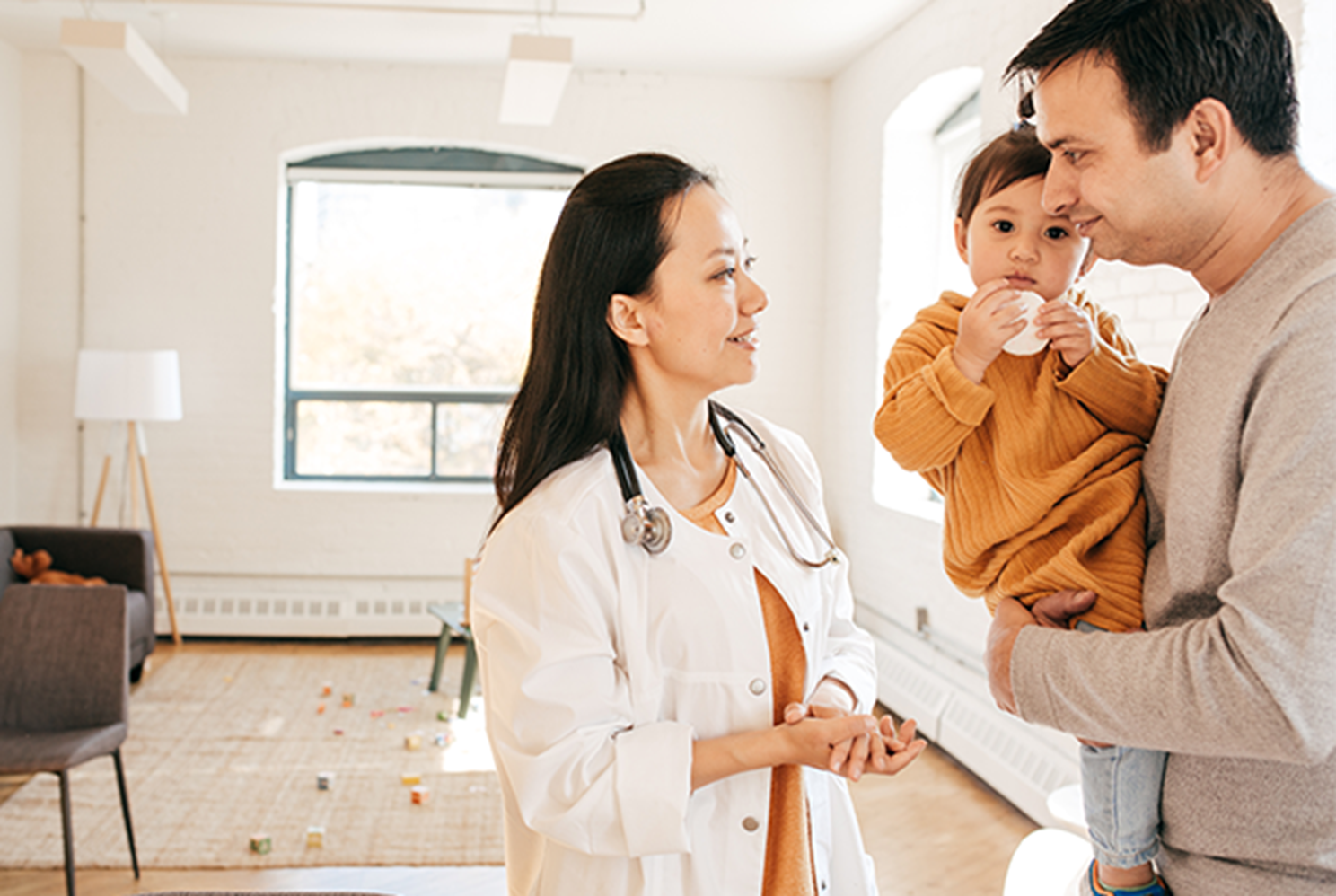 Parent holds young toddler while talking to Doctor