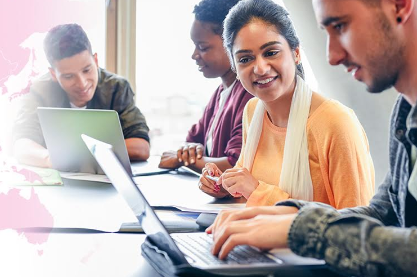 Diverse group of young adults sitting around table working on laptops
