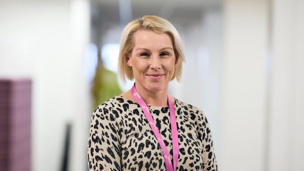 A Reckitt employee in a branded lanyard smiles at the camera