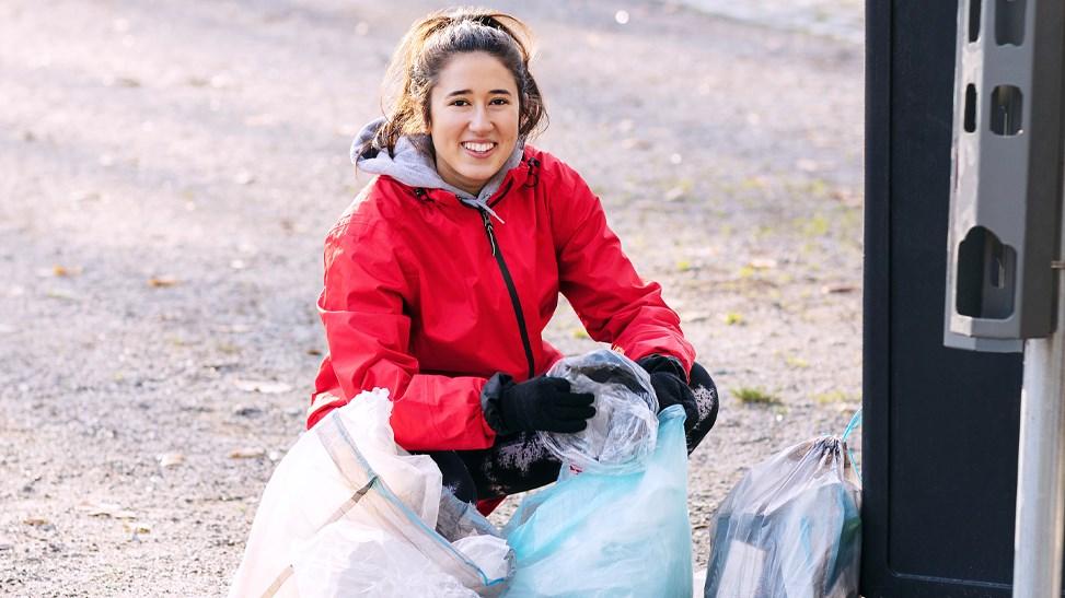 Female volunteer collecting plastics in the park next to the rubbish bin.