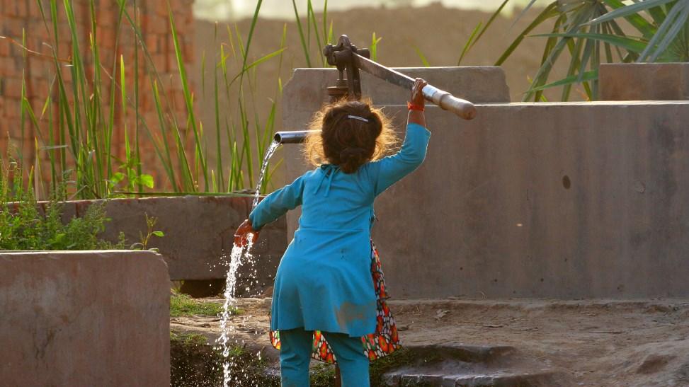 A little girl is getting water after pumping the manual hand pump.