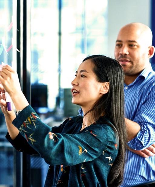 Businesswoman sticking notes on glass with colleague