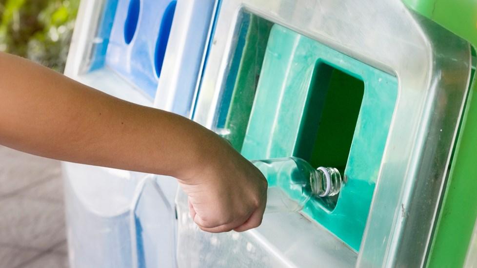 A young person putting a bottle into the recycling bin.