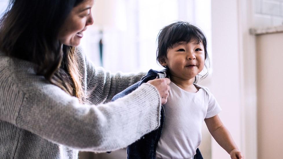 A Mother helping her young daughter put on her coat.