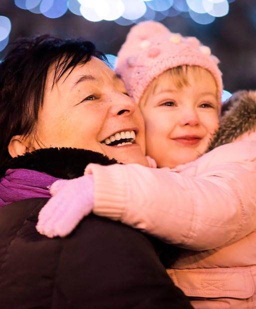 Grandmother hugging with granddaughter outdoor with Christmas street lights in background