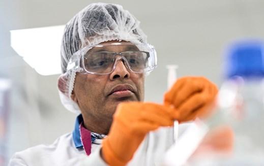 A Reckitt employee in a hairnet, safety glasses and gloves examines a tube.