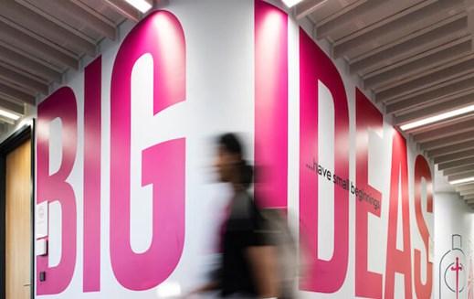 A person is walking through the Reckitt office hallway, past words on the wall that say "Big ideas have small beginnings"