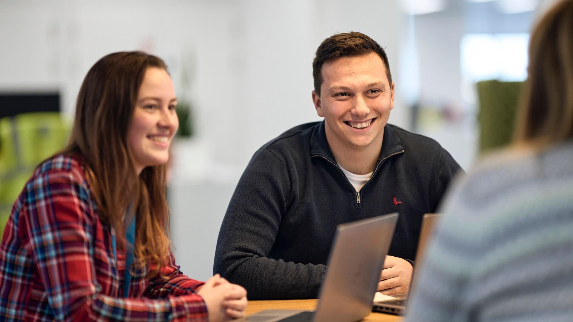 Reckitt employees with open laptops, in a conversation at a table in the Reckitt office in Slough.