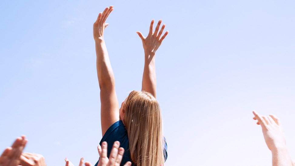 Woman with arms raised above a crowd.