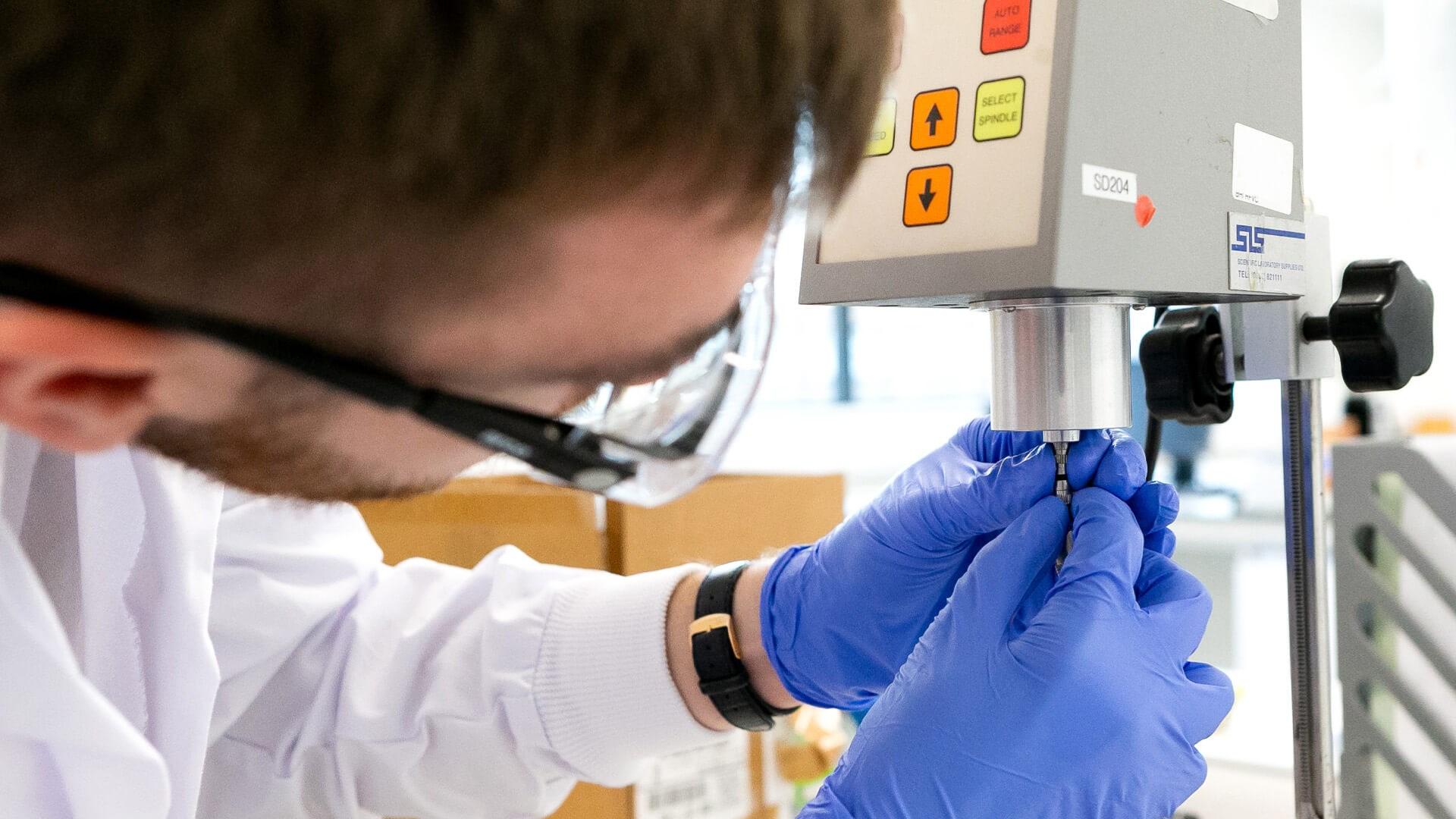 A Reckitt employee in lab safety gear works on a machine